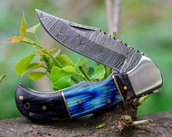 May include: A folding pocket knife with a blue and black wood handle and a stainless steel blade with a damascus pattern.