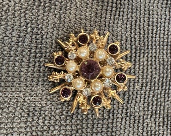 Vtg gold-tone starburst brooch pin featuring purple rhinestones and faux pearls.