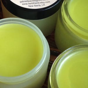 Pu&ograve; includere: Tre barattoli di vetro pieni di un balsamo giallo brillante. I barattoli sono su una superficie di legno.