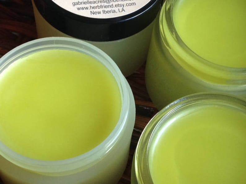 Pu&ograve; includere: Tre barattoli di vetro pieni di un balsamo giallo brillante. I barattoli sono su una superficie di legno.