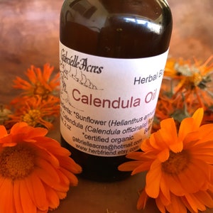 A 2oz bottle of calendula oil surrounded by fresh and dry calendula flowers.