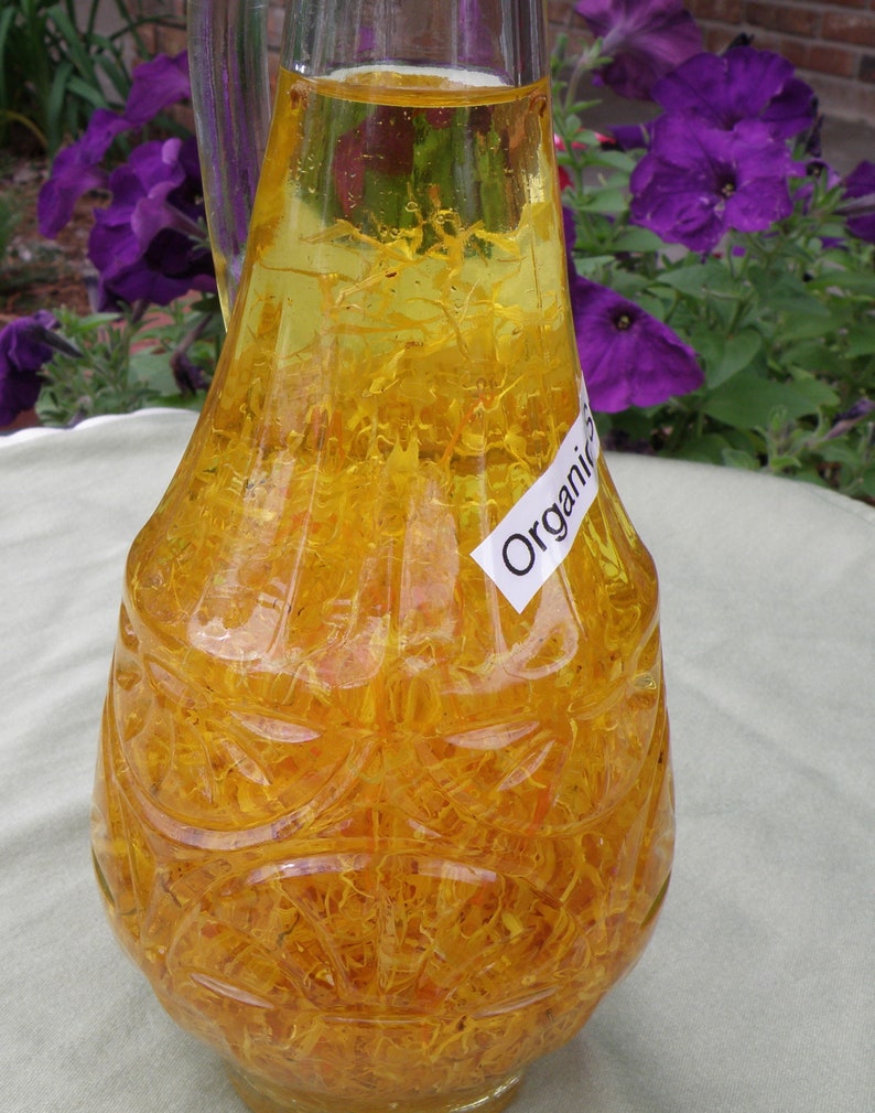 Pu&ograve; includere: Una bottiglia di vetro trasparente con una superficie testurizzata riempita di un liquido giallo e petali di fiori gialli. La bottiglia ha un'etichetta che dice "Organic".