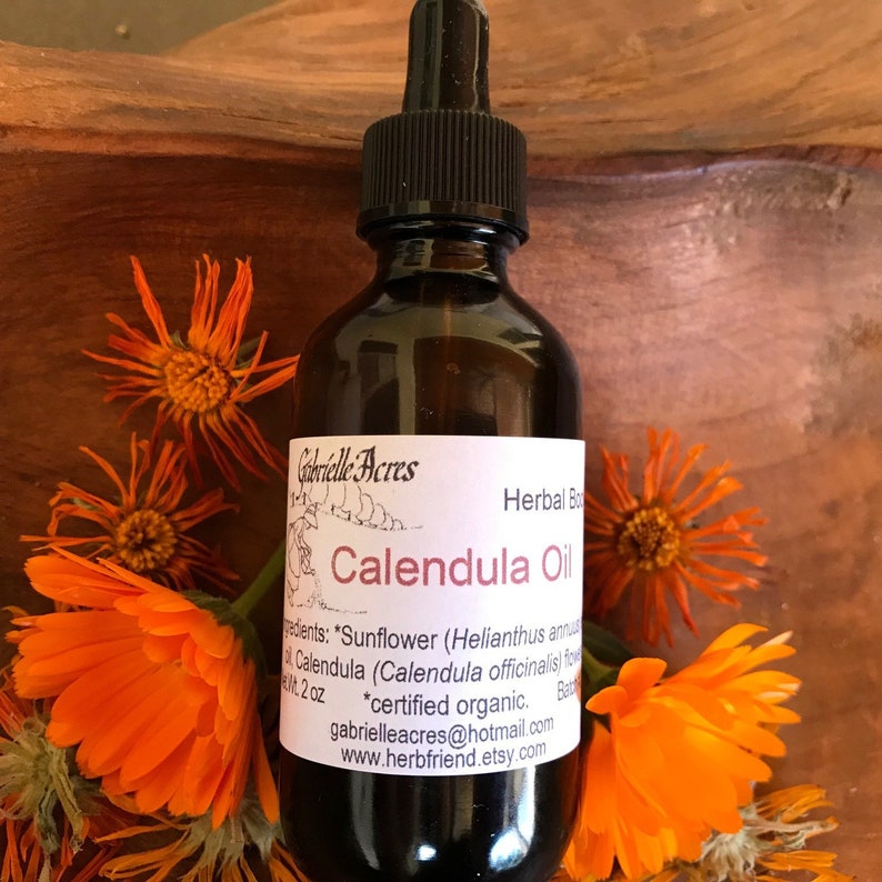 A 2 oz amber bottle with dropper of calendula salve on a brown wooden board surrounded by orange calendula flowers