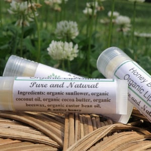 May include: Three organic lip balm tubes with white labels. The label on the front tube reads "Pure and Natural" and lists the ingredients. The label on the back tube reads "Honey Bee Natural Organic Lip Balm" and says "Pure and Natural".