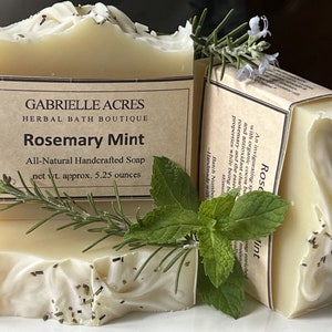May include: Two bars of handmade soap with the label "Rosemary Mint" and the text "Gabrielle Acres Herbal Bath Boutique". The soap is light in color, with sprigs of rosemary and mint leaves. The net weight is approximately 5.25 ounces.