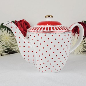 May include: White ceramic teapot with red polka dots and a red lid. The lid has a gold knob and a striped design. The teapot has a curved spout and handle. A decorative item for the kitchen.