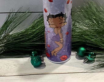 May include: A stainless steel tumbler with a purple and white design featuring a cartoon character with black hair and a red lip. The tumbler has a clear lid and a straw.