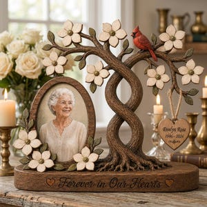 May include: A memorial photo frame featuring a sculpted tree with white dogwood flowers and a red cardinal. An oval frame holds a portrait of an elderly person. A heart-shaped wooden tag reads Evelyn Rose 1946-2024. The base says Forever in Our Hearts.