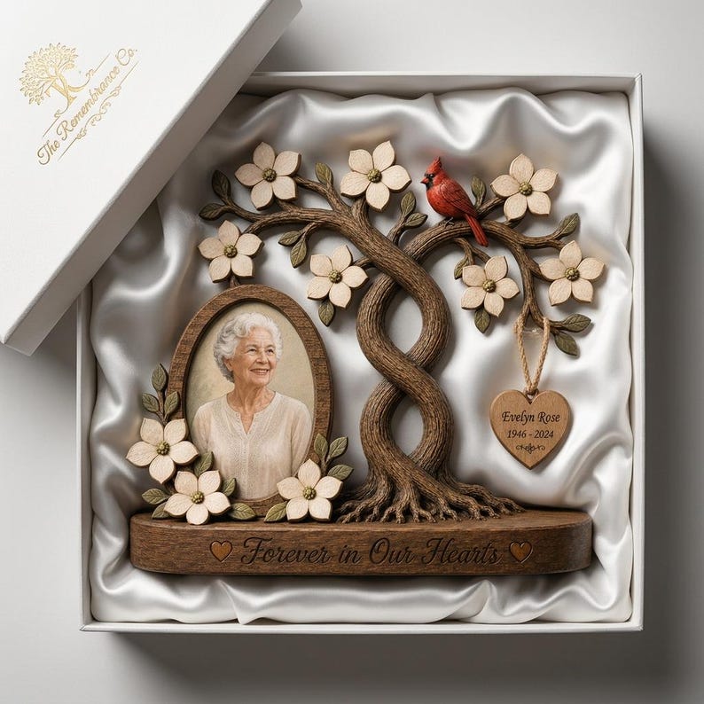 May include: A memorial photo frame featuring a sculpted brown tree with white flowers and a red cardinal. An oval frame holds a portrait of an older person. A heart-shaped wooden tag reads Evelyn Rose 1946-2024. The base says Forever in Our Hearts.