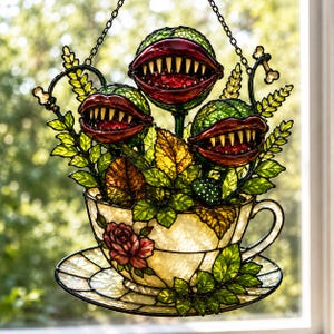 May include: A stained glass suncatcher featuring three carnivorous plants with red lips and sharp teeth emerging from a cream-colored teacup and saucer. The teacup is decorated with a red rose and green leaves, suspended by a black metal chain.