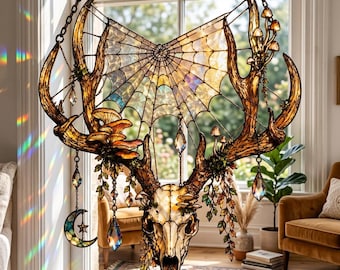 May include: A stained glass suncatcher featuring a deer skull with large antlers, a central spiderweb design, and hanging crystal prisms. The piece includes small mushroom accents, hanging crescent moon and star charms, and green leaf details.