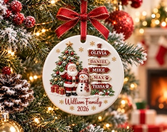 May include: A round white ceramic Christmas ornament featuring a decorated tree, Santa Claus, and a snowman. A red ribbon hangs from the top. A signpost lists the names Olivia, Daniel, Mike, Max, and Tessa. The text William Family 2026 is printed below.