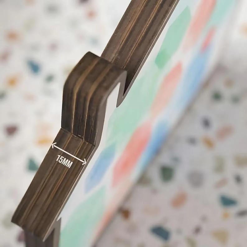 May include: A dark brown wooden object with a layered edge profile measuring 15mm in thickness. The front surface features a soft, abstract pattern of light blue, peach, and mint green shapes on a white background, viewed from an angled perspective.