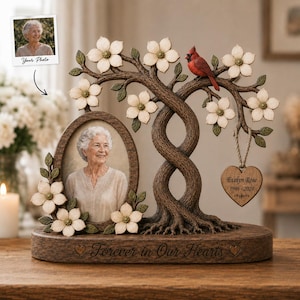 May include: A memorial photo frame featuring a sculpted tree with white dogwood flowers and a red cardinal. An oval frame holds a portrait of an older person. A heart-shaped wooden tag reads Evelyn Rose 1946-2024. The base says Forever in Our Hearts.