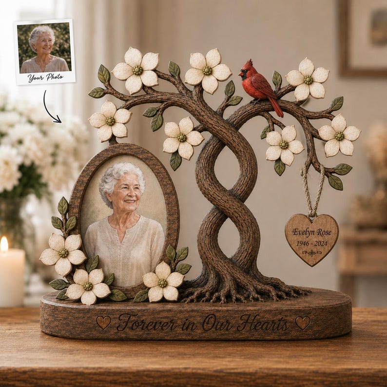 May include: A memorial photo frame featuring a sculpted tree with white dogwood flowers and a red cardinal. An oval frame holds a portrait of an older person. A heart-shaped wooden tag reads Evelyn Rose 1946-2024. The base says Forever in Our Hearts.