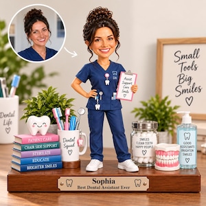 Op de afbeelding: Een gepersonaliseerde bobblehead-figuur van een tandartsassistent in marineblauw uniform, met een klembord met de tekst 'Assist Support Care Smile'. De basis heeft een plaatje met 'Sophia Best Dental Assistant Ever' en tandiconen.