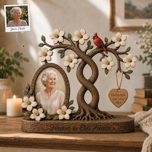 May include: A memorial photo frame featuring a sculpted tree with white dogwood flowers and a red cardinal. An oval frame holds a portrait, while a heart-shaped wooden ornament hangs from a branch with the text Evelyn Rose 1946-2024. The base reads Forever in Our Hearts.