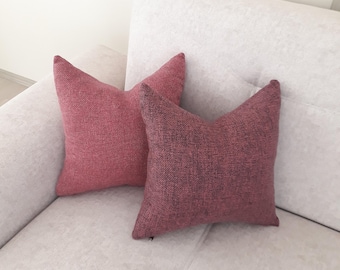 Può includere: Due cuscini decorativi rosso-rosa poggiano su un divano grigio chiaro. I cuscini hanno un aspetto strutturato e una forma appuntita a stella. Il divano è di colore neutro e dal design semplice.