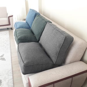 Könnte beinhalten: Ein modernes Sofa mit hellbeigem Untergestell und mehreren quadratischen Kissen in Blau- und Grautönen. Die Kissen sind auf dem Sofa angeordnet und bieten eine komfortable Sitzgelegenheit. Das Sofa hat ein minimalistisches Design.