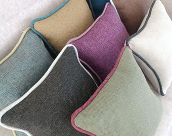 Könnte beinhalten: Eine Sammlung rautenförmiger Zierkissen in verschiedenen Farben wie Türkis, Beige, Lila, Braun und Grau. Jedes Kissen hat eine kontrastierende Bordüre in Farben wie Weiß, Türkis und Rosa, die auf einem neutralen Sofa arrangiert sind.