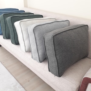 May include: A row of five rectangular throw cushions with piped edges, arranged in a line. The cushions feature a textured fabric finish and come in a gradient of colours including dark blue, dark green, off-white, light grey, and dark charcoal grey.