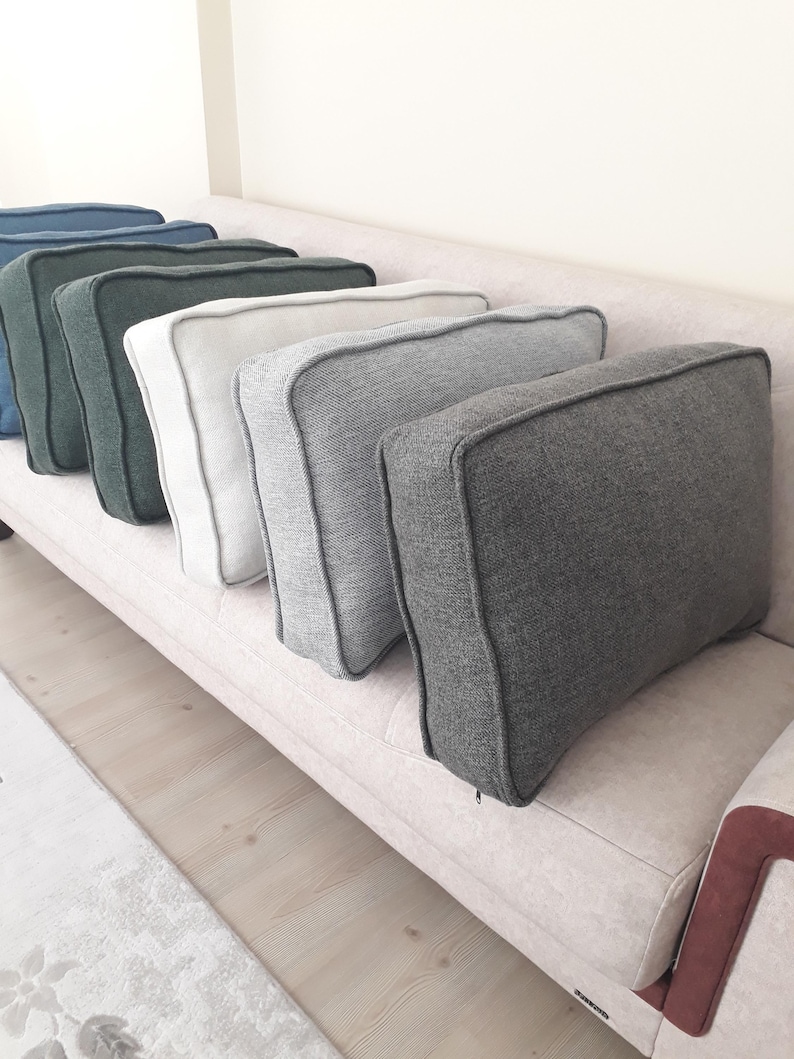 May include: A row of five rectangular throw cushions with piped edges, arranged in a line. The cushions feature a textured fabric finish and come in a gradient of colours including dark blue, dark green, off-white, light grey, and dark charcoal grey.