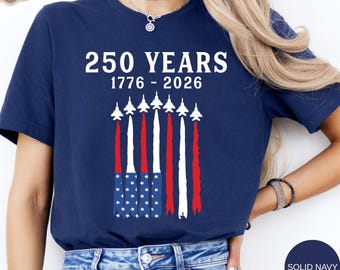 May include: Navy blue t-shirt with the text "250 YEARS 1776 - 2026" in white. The design includes an American flag with jets leaving red, white, and blue contrails. The shirt is a solid navy color.