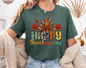 May include: A green t-shirt featuring a Thanksgiving turkey design with the words "Happy Thanksgiving". The turkey has a leopard print pattern and is surrounded by red and orange leaves. The text is in various colors and patterns.