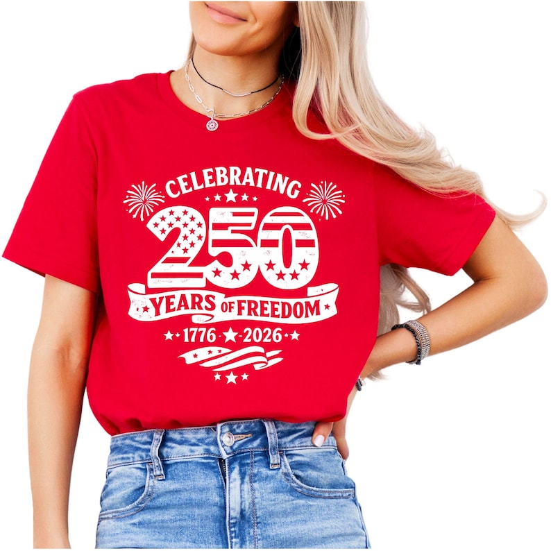 May include: A bright red short-sleeved t-shirt featuring a white graphic print that reads CELEBRATING 250 YEARS OF FREEDOM 1776-2026. The design includes large numbers filled with stars and stripes, firework icons, and a waving American flag motif.