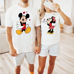A man and a woman are standing together, both wearing white t-shirts with Mickey Mouse designs.