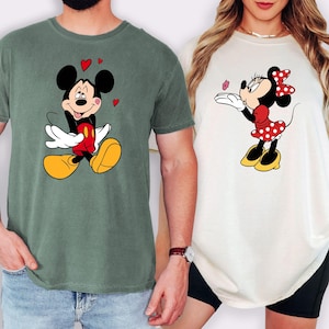 A man and a woman are standing next to each other, both wearing t-shirts with Mickey Mouse designs.