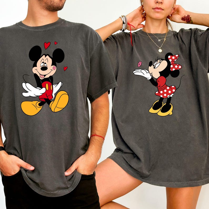 A man and a woman are standing next to each other, both wearing gray t-shirts with Mickey Mouse and Minnie Mouse designs.