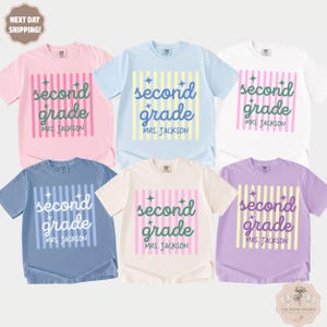 May include: Six short-sleeve crew neck t-shirts in pink, light blue, white, blue, cream, and lavender. Each shirt features a vertical striped background with the text second grade and MRS. JACKSON printed in a script font with star accents.