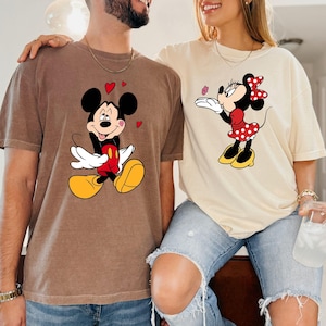 A man and a woman are standing close together, both wearing t-shirts with Mickey Mouse designs.