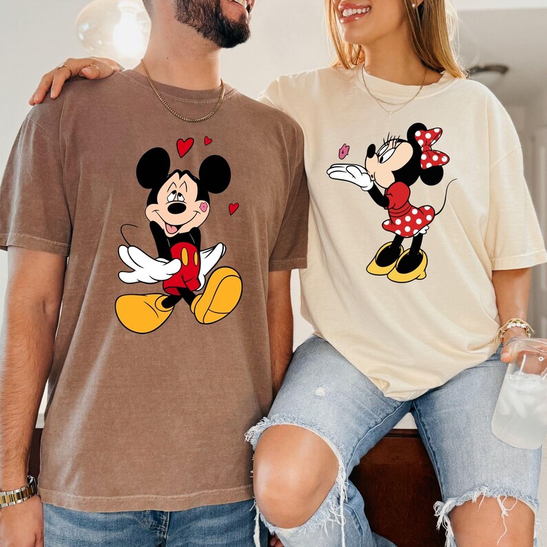 A man and a woman are standing close together, both wearing t-shirts with Mickey Mouse designs.