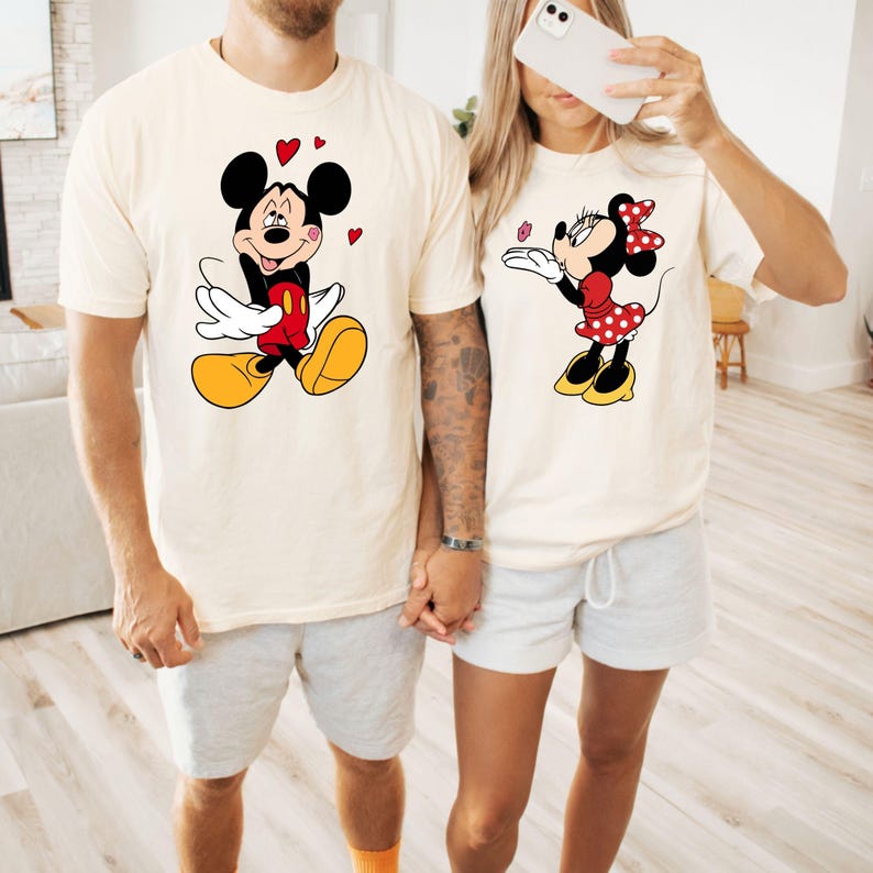 A man and a woman are standing together, both wearing Mickey Mouse-themed t-shirts.