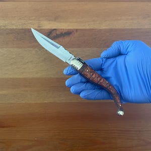 May include: A small, silver pocket knife with a brown, patterned handle. The knife is open and the blade is visible.