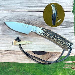 May include: A hunting knife with a light-colored blade and a handle made of brown and white patterned material. The knife has a black leather lanyard and is displayed with a small sheath. The text "Joker" and "Flecha" is visible on the blade.