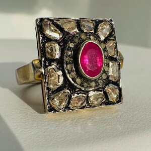 May include: A silver ring with a square-shaped setting featuring a large ruby surrounded by smaller diamonds.