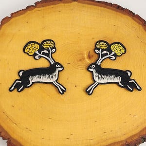 Może przedstawiać: Dwa czarne i białe haftowane naszywki z ozdobnym królikiem z żółtymi akcentami kwiatowymi na drewnianej powierzchni.