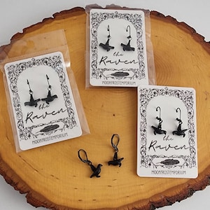 May include: Three pairs of black raven earrings on white cards with the text "the raven" and "moonfrostemporium".
