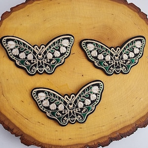 May include: Three embroidered green and black butterfly patches with gold accents. The butterflies have white flower details and a black eye design.