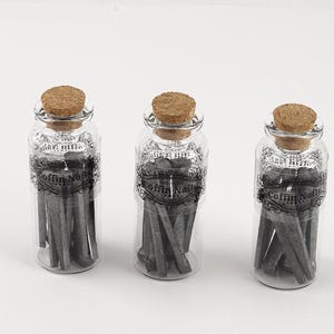 May include: Three clear glass bottles with cork stoppers, each filled with gray coffin nails. The bottles have decorative labels with the text "Coffin Nails". The background is plain white.