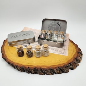 May include: A collection of small glass bottles with cork stoppers, filled with various materials, arranged on a wooden slab. The bottles are labeled and come with a metal tin featuring a celestial design. A second metal tin with elemental symbols is also present.
