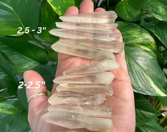 May include: A collection of clear quartz crystal points, ranging in size from 2-2.5 inches and 2.5-3 inches. The points are arranged in a stack, with the largest points at the bottom and the smallest points at the top.