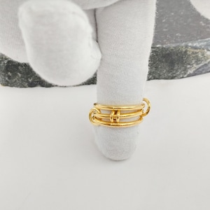 May include: A gold ring with a distinctive design. The ring has three bands joined by small, circular links. The ring is shown on a white surface, highlighting its intricate details and polished finish.