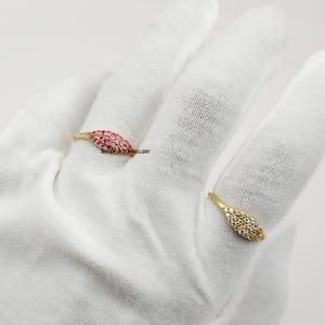 Puede incluir: Dos anillos de oro con diseños en forma de hoja. Un anillo presenta piedras preciosas rosas, el otro tiene piedras preciosas claras. Los anillos se muestran sobre una superficie blanca. El texto "SKYWORLDJEWELLERY" es visible.