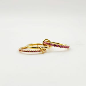 Peut inclure: Trois bagues en or avec des pierres pr&eacute;cieuses roses. Une bague est orn&eacute;e de pierres roses, une autre a un design de n&oelig;ud et la troisi&egrave;me est une bande simple. Les bagues sont sur fond blanc.