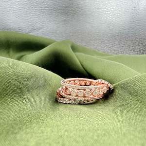 Op de afbeelding: Een stapel roségouden ringen met sprankelende diamantaccenten. De ringen zijn geplaatst op een groene stof, wat een luxueuze en elegante presentatie creëert. De diamanten zijn in verschillende patronen gezet, wat het ingewikkelde ontwerp van de ringen benadrukt.