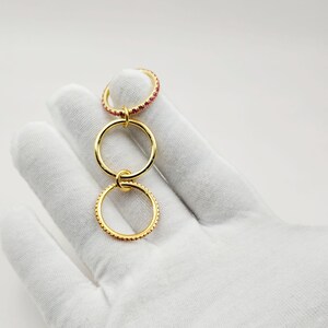 Peut inclure: Un ensemble de bagues dor&eacute;es avec trois anneaux reli&eacute;s. L'anneau sup&eacute;rieur est incrust&eacute; de petites pierres pr&eacute;cieuses rouges. Les deux autres anneaux sont en or uni. Les anneaux sont reli&eacute;s par de petites boucles dor&eacute;es.